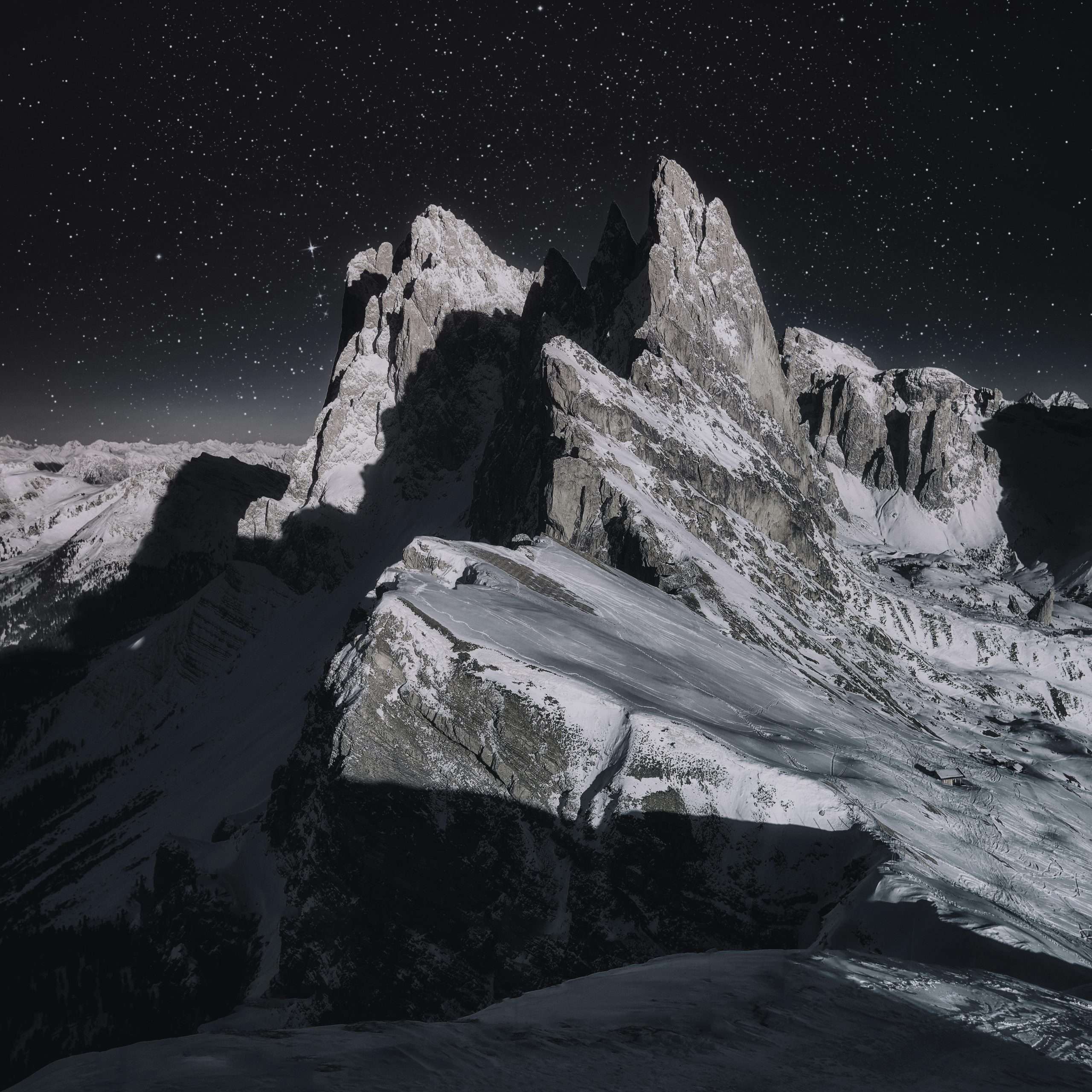 Dramatic night view of snow-capped peaks in the Italian Alps under a starry sky.