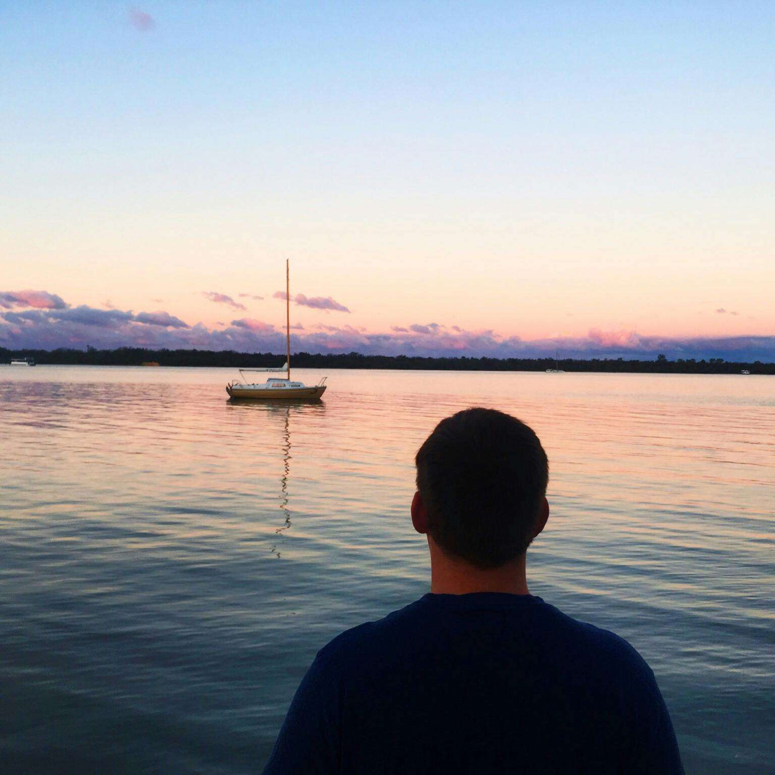 A serene view of a person watching a sailboat at sunset in Labrador, Queensland.