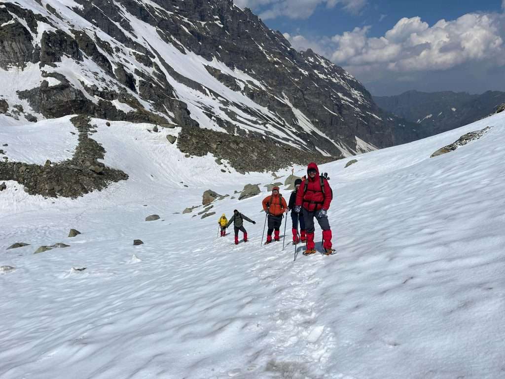 Adventurers trekking through snow in Hampta Pass, Himalayas. Experience majestic alpine scenery.